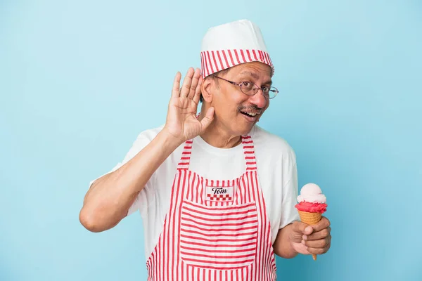 Senior american ice cream man holding an ice cream isolated on blue background trying to listening a gossip.