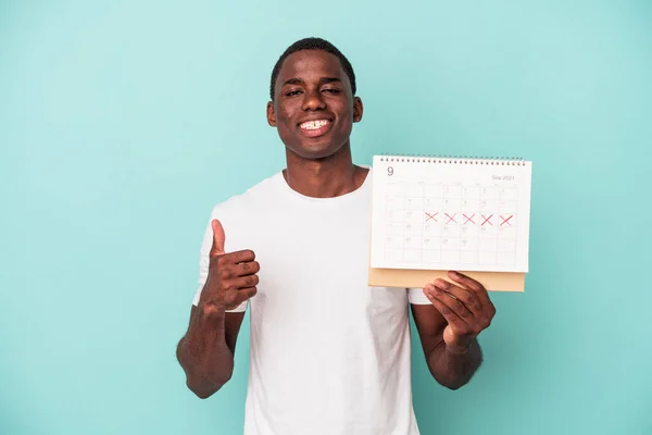 青い背景の笑顔と親指を上げる上で隔離されたカレンダーを保持する若いアフリカ系アメリカ人男性 — ストック写真
