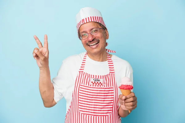 Senior american ice cream man holding an ice cream isolated on blue background joyful and carefree showing a peace symbol with fingers.