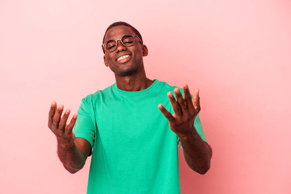 Young African American man isolated on pink background showing a welcome expression.