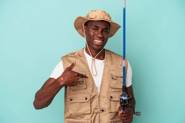年轻的非洲裔美国渔民拿着钓竿 与蓝色背景的人隔离 手指衬衫的复制品空间 自豪而自信 — 图库照片