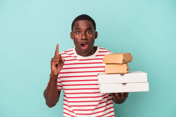 Joven Afroamericano Sosteniendo Pizzas Hamburguesas Aisladas Sobre Fondo Azul Teniendo —  Fotos de Stock