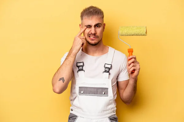 Young painter man isolated on yellow background showing a disappointment gesture with forefinger.