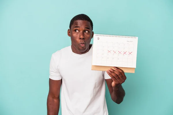 Молодой Афроамериканец Держащий Календарь Синем Фоне Пожимает Плечами Закрывает Глаза — стоковое фото