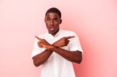 Genç Afrikalı Amerikalı adam pembe arka planda iki seçenek arasında seçim yapmaya çalışıyor..