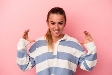 Pembe arka planda izole edilmiş genç Rus kadın iki eliyle bir şey tutuyor, ürün sunumu..