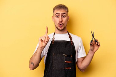 Young caucasian hairdresser man holding scissors isolated on yellow background having some great idea, concept of creativity.