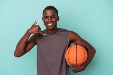 Genç Afro-Amerikalı bir adam mavi arka planda izole edilmiş bir şekilde basketbol oynuyor..