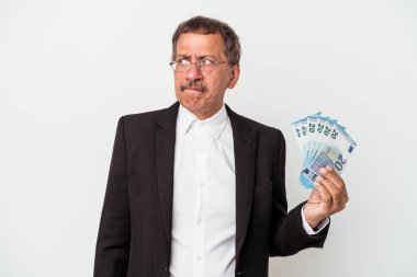 Middle aged indian business man holding bills isolated on white background confused, feels doubtful and unsure.