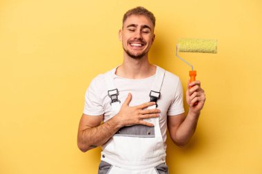 Young painter man isolated on yellow background laughing and having fun.