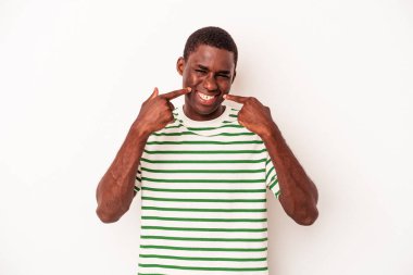 Beyaz arka planda izole edilmiş genç Afrikalı Amerikalı adam gülümsüyor, parmaklarını ağıza doğrultuyor..