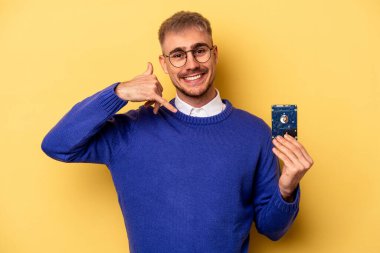 Young computer man isolated on yellow background showing a mobile phone call gesture with fingers.