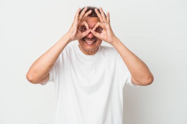 Middle aged indian man isolated on white background showing okay sign over eyes