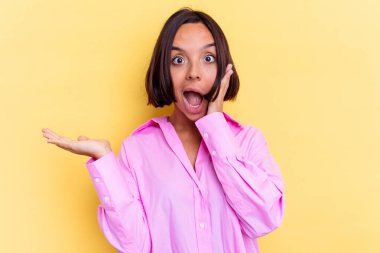 Sarı arka planda izole edilmiş genç melez kadın avuç içinde fotokopi alanı tutuyor, el üstünde tutuyor. Şaşırmış ve mutlu..