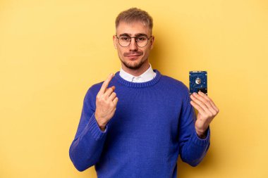 Young computer man isolated on yellow background pointing with finger at you as if inviting come closer.