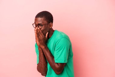 Genç Afrikalı Amerikalı bir adam pembe arka planda izole edilmiş bir şekilde bir şeylere gülüyor, elleriyle ağzını kapatıyor..