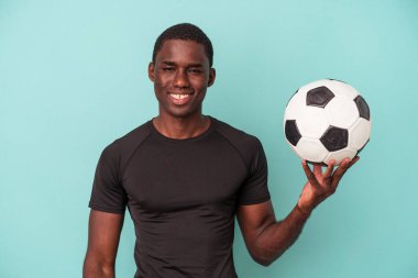 Futbol oynayan genç Afrikalı Amerikalı adam mavi arka planda izole edilmiş mutlu, güler yüzlü ve neşeli..