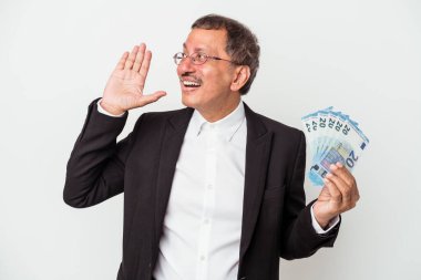 Middle aged indian business man holding bills isolated on white background shouting and holding palm near opened mouth.