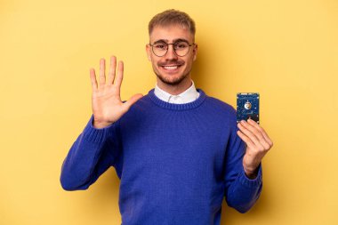Young computer man isolated on yellow background smiling cheerful showing number five with fingers.