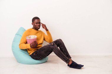 Beyaz arka planda izole edilmiş patlamış mısır yiyen genç Afrikalı Amerikalı adam işaret parmağıyla yaptığı hayal kırıklığı jestini gösteriyor..