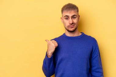 Sarı arka planda izole edilmiş genç beyaz adam işaret parmağıyla fotokopi alanını işaret ederek şok oldu..