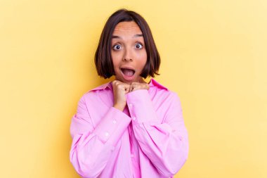 Genç melez kadın sarı arka planda izole edilmiş şans için dua ediyor, şaşırmış ve ağzı açık bir şekilde önüne bakıyor..