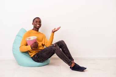 Genç Afrikalı Amerikalı bir adam beyaz arka planda izole edilmiş patlamış mısır yiyor. Bir avuç içinde fotokopi alanı ve belinde başka bir el tutuyor..