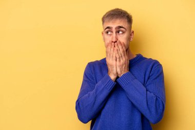 Kafkasyalı genç adam sarı arka planda izole edilmiş. Düşünceli bir şekilde, ağzını eliyle kapatan bir fotokopi odasına bakıyor..