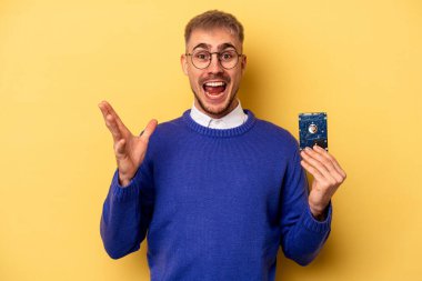 Young computer man isolated on yellow background receiving a pleasant surprise, excited and raising hands.