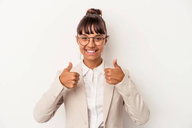 Genç melez bir kadın beyaz arka planda izole edilmiş. Baş parmağını kaldırıyor, gülümsüyor ve kendinden emin..