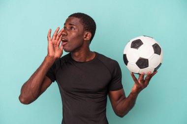 Futbol oynayan genç Afrikalı Amerikalı adam mavi arka planda izole edilmiş bağırıyor ve avuç içini açık tutuyor..