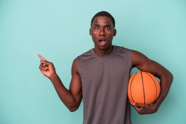 Basketbol oynayan Afro-Amerikalı genç bir adam mavi arka planda izole edilmiş.