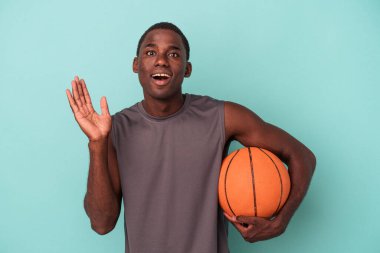 Basketbol oynayan genç Afro-Amerikalı adam mavi arka planda izole edilmiş, şaşırmış ve şok olmuş..
