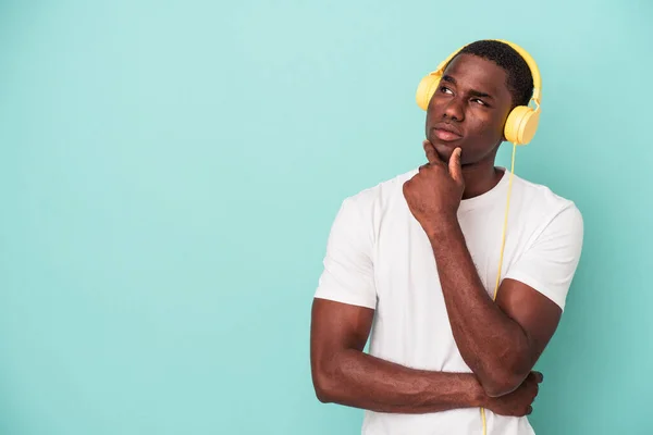 若いアフリカ系アメリカ人の男性は 疑いと懐疑的な表現で横に見える青い背景に隔離された音楽を聞いて — ストック写真