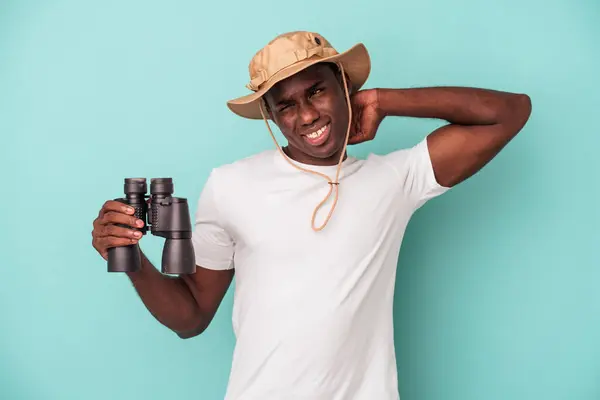 年轻的非洲裔美国人手持双筒望远镜 蓝色背景隔离 后脑勺接触 思考并做出选择 — 图库照片