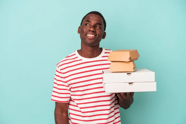 Молодой Афроамериканец Держащий Пиццу Бургеры Голубом Фоне Мечтает Достижении Целей — стоковое фото