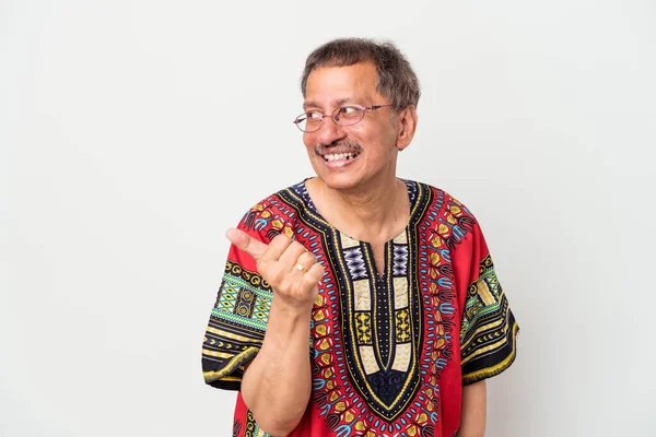 Senior indian man wearing a Indian costume isolated on white background points with thumb finger away, laughing and carefree.