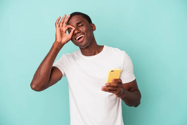年轻的非裔美国人拿着一部蓝色背景的手机 兴奋得目瞪口呆 — 图库照片