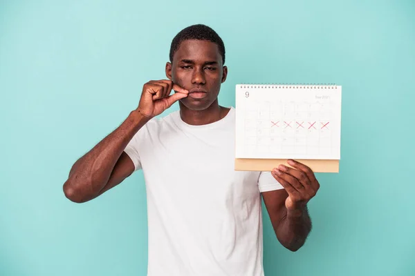 Mladý Afroameričan Drží Kalendář Izolovaný Modrém Pozadí Prsty Rtech Drží — Stock fotografie