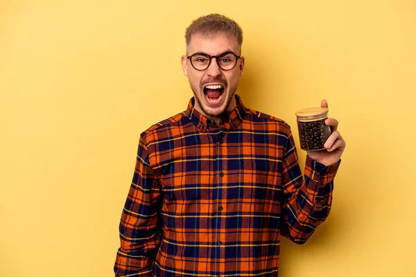 Young Caucasian Man Holding Coffee Jar Isolated Yellow Background Screaming — Stock fotografie