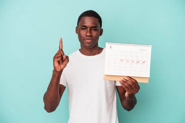 Mladý Afroameričan Drží Kalendář Izolované Modrém Pozadí Ukazující Číslo Jedna — Stock fotografie