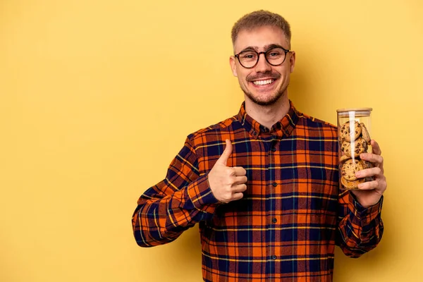 Young Caucasian Man Holding Cookies Jar Isolated Yellow Background Smiling — Stockfoto