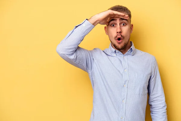 Young caucasian man isolated on yellow background looking far away keeping hand on forehead.