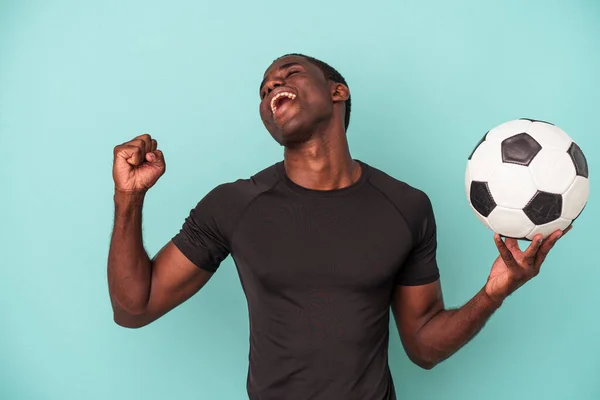 Młody Afroamerykanin Gra Piłkę Nożną Niebieskim Tle Podnosząc Pięść Zwycięstwie — Zdjęcie stockowe