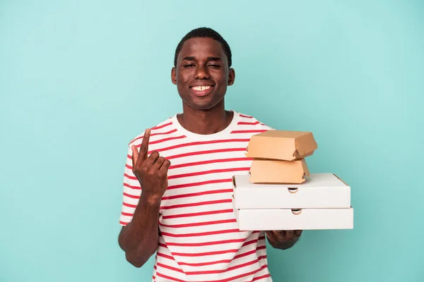Молодой Афроамериканец Держащий Пиццу Бургеры Голубом Фоне Указывая Пальцем Тебя — стоковое фото
