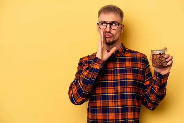 Junger Kaukasischer Mann Hält Ein Mandelglas Isoliert Auf Gelbem Hintergrund — Stockfoto