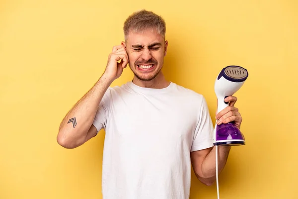 Young Caucasian Man Holding Iron Isolated Yellow Background Covering Ears — Stock Photo, Image