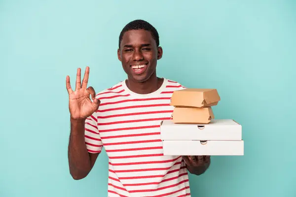 Mladý Afroameričan Drží Pizzy Hamburgery Izolované Modrém Pozadí Veselý Sebevědomý — Stock fotografie