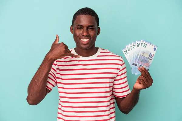 青の背景に隔離された銀行券を持っている若いアフリカ系アメリカ人男性指で携帯電話の呼び出しジェスチャーを示す — ストック写真