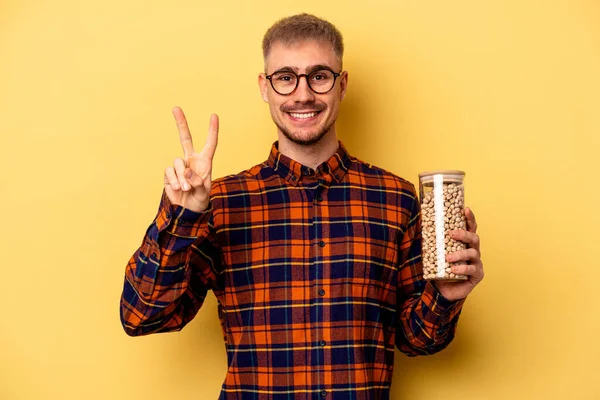 Young Caucasian Man Holding Chickpeas Isolated Yellow Background Showing Number — Stock fotografie